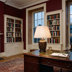 Elstead Morris Small Table Lamp in Black Gold lit on a desk in an oxblood red Georgian study