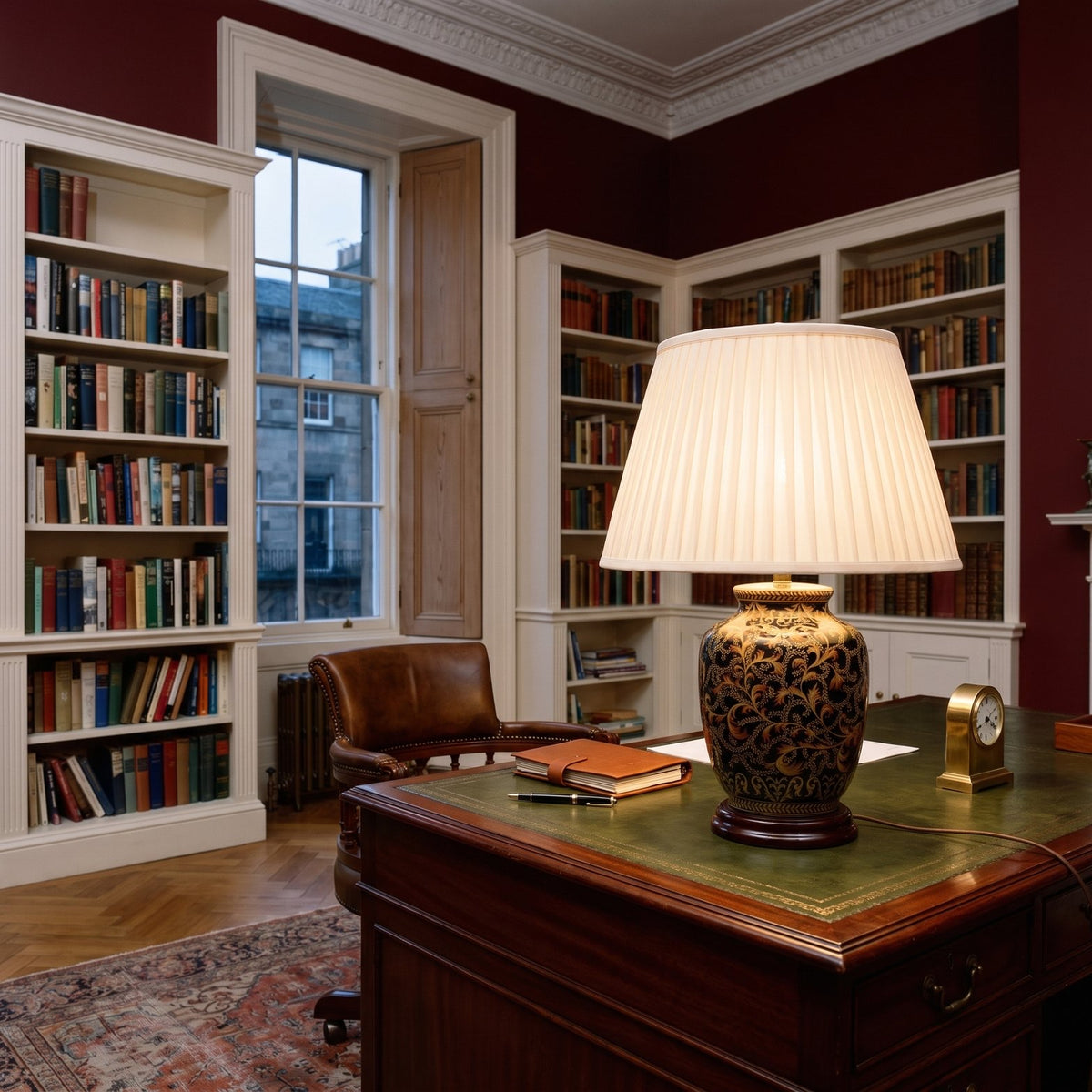 Elstead Morris Small Table Lamp in Black Gold lit on a desk in an oxblood red Georgian study