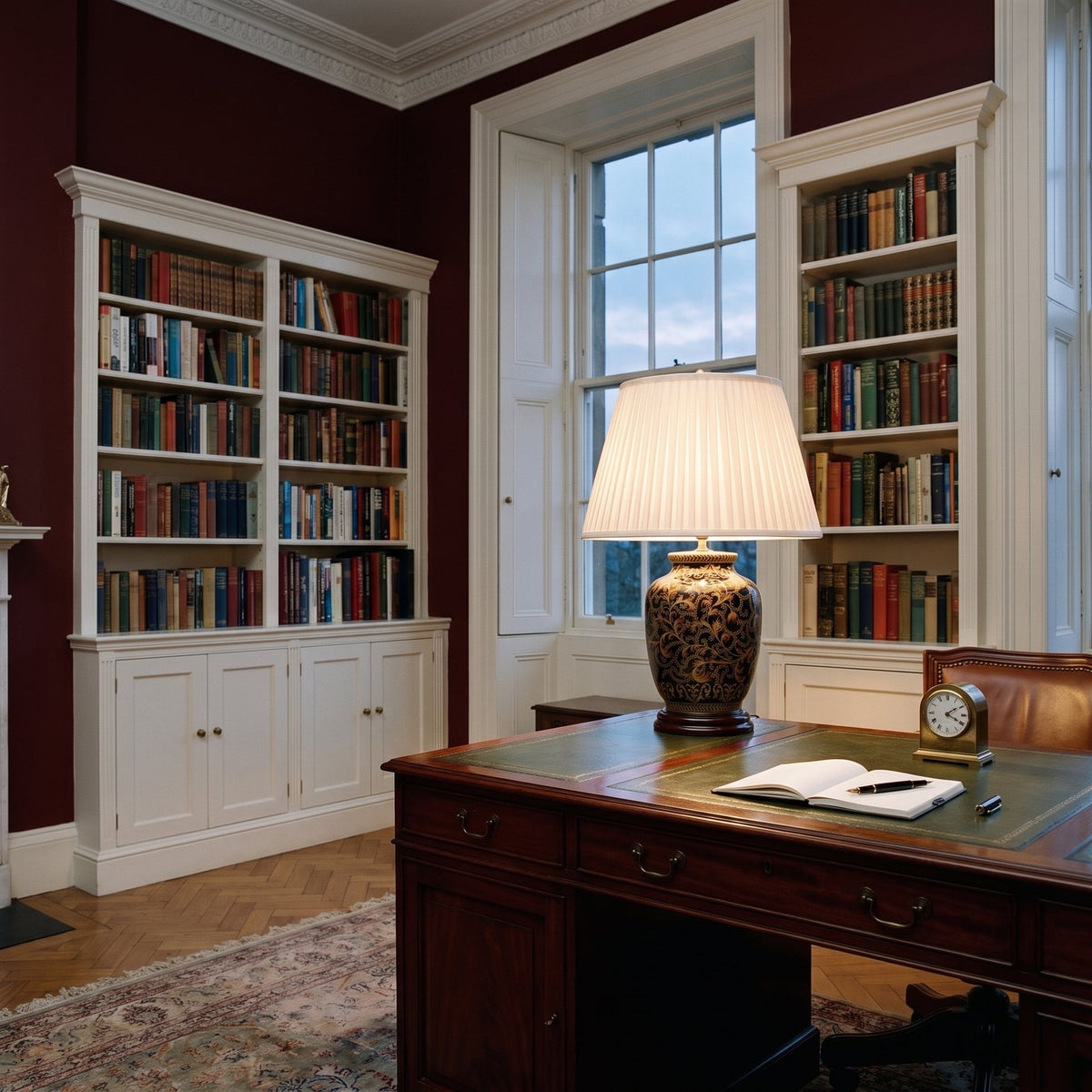 Elstead Morris Small Table Lamp in Black Gold lit on a desk in an oxblood red Georgian study