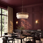 Marietta Grand 7 light pendant in antique brass over a dining table, with Marietta wall lights on an oxblood panelled wall