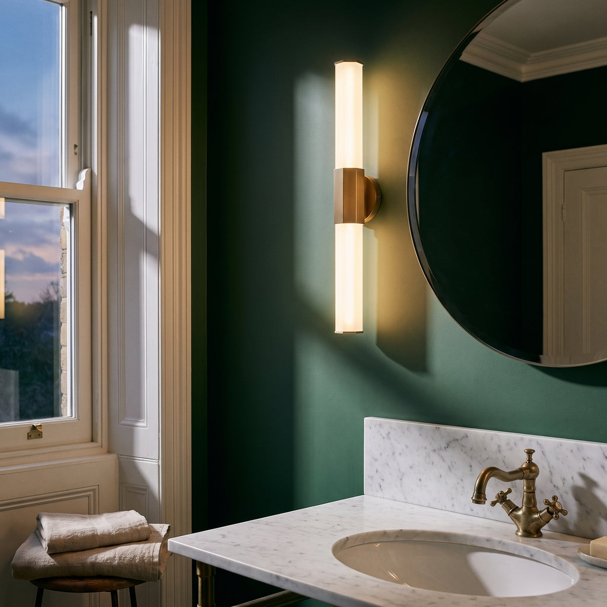 Quintiesse Facet Bathroom Dual LED Wall Light in Heritage Brass, lit, in a styled room. Editorial image for the Antique Brass Bathroom Lights collection.