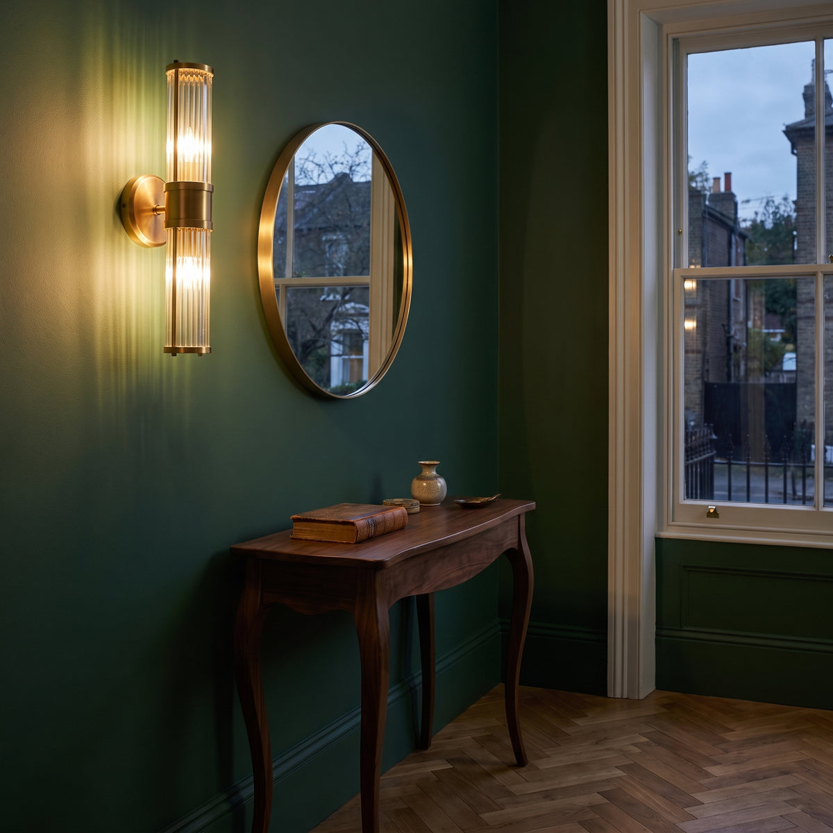Eichholtz Claridges Double Wall Light in Antique Brass Finish with Glass Shade, lit, in a styled room. Editorial image for the Antique Brass Wall Lights collection.