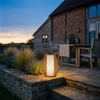 Mandalay solar and rechargeable lantern in corten aluminium lit on a York stone terrace beside a converted barn at dusk