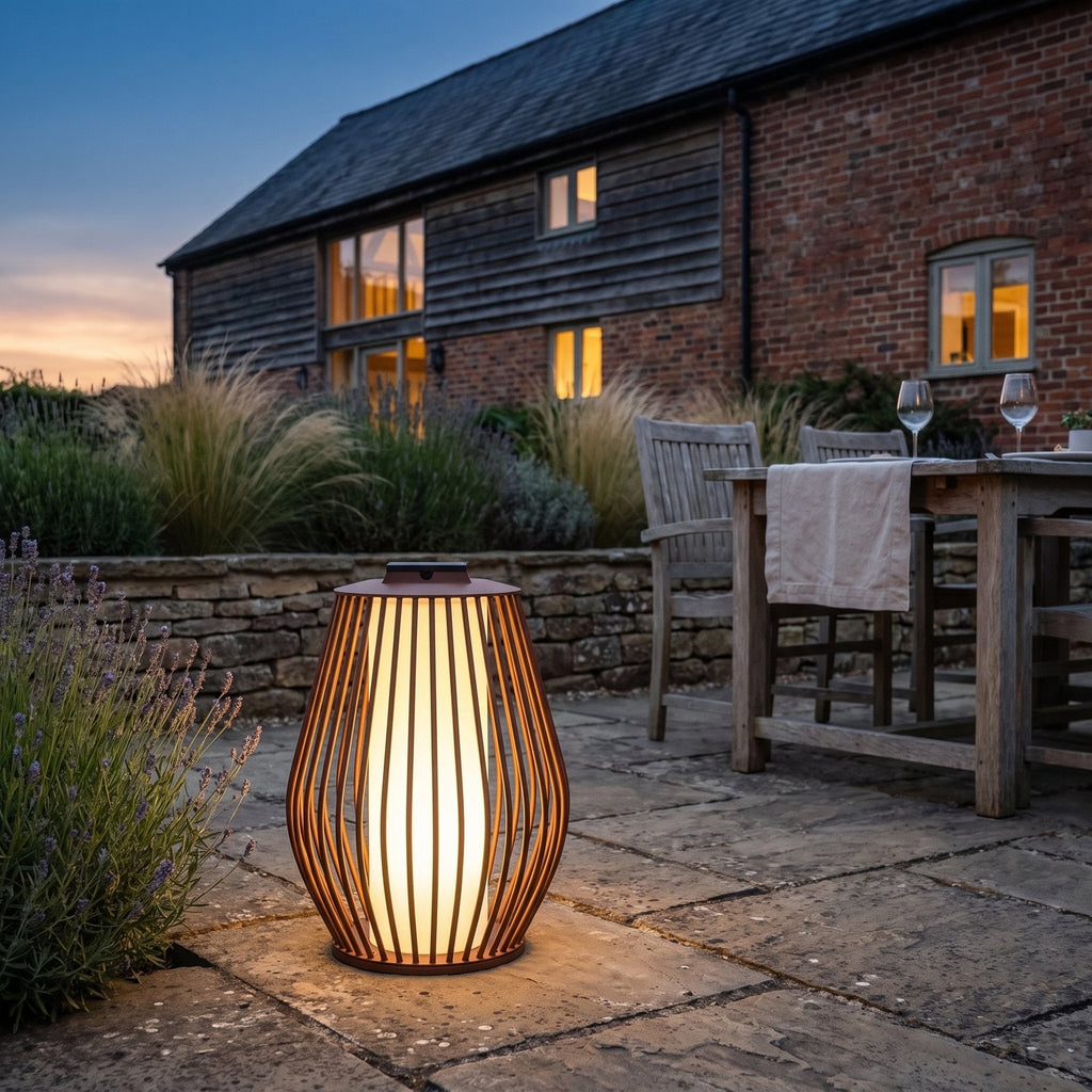 Mandalay solar and rechargeable lantern in corten aluminium lit on a York stone terrace beside a converted barn at dusk