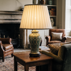 A cozy, traditional living room featuring a decorative green ceramic table lamp on a wooden side table with leather chairs.